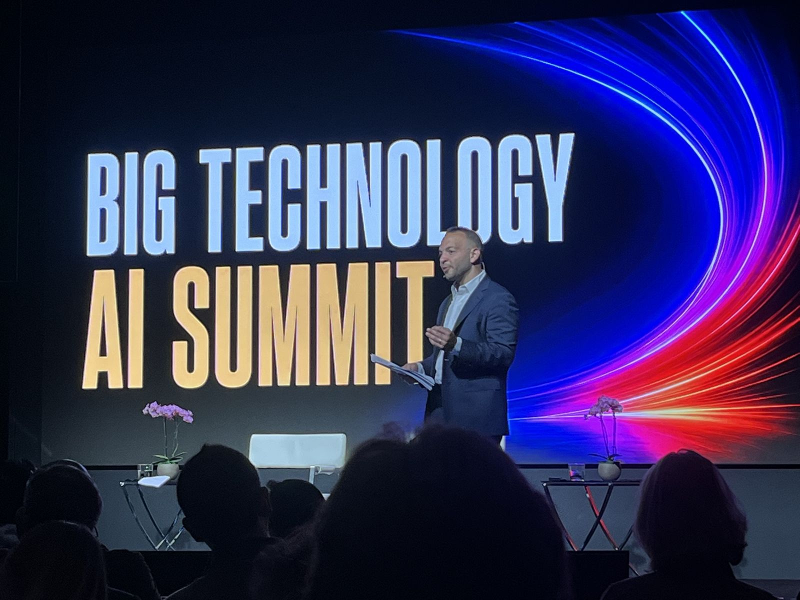 Host on stage opening the Big Technology AI Summit, large title screen behind